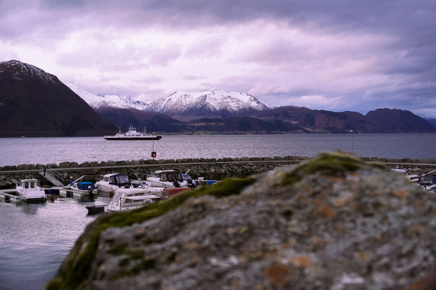 Boats dock at a stone pier before snowy mountain peaks.