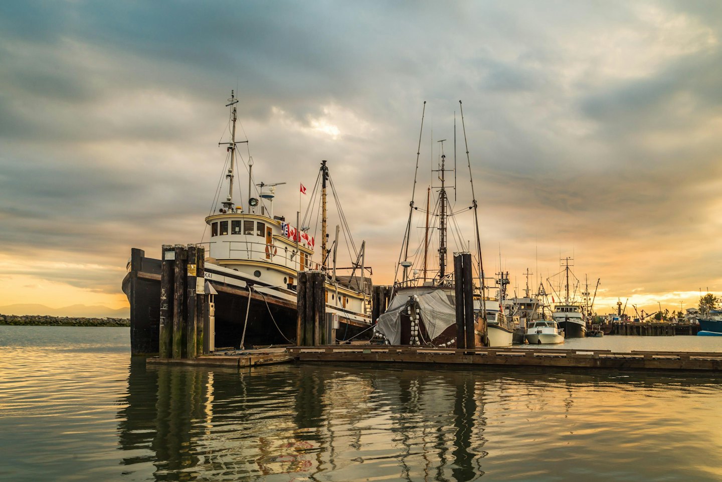 Fishing boats docked at a wooden pier near mountains.