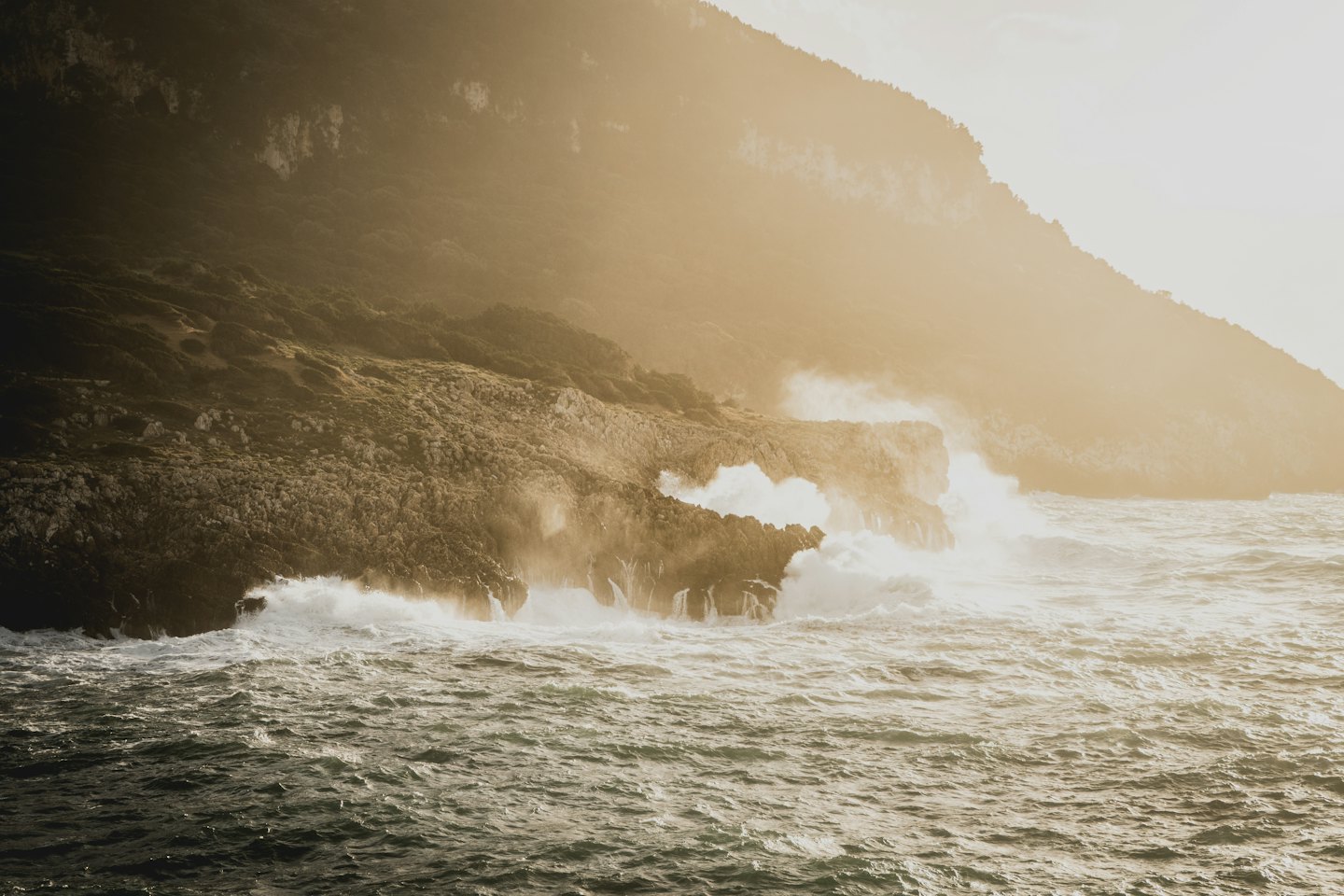 Ocean waves crash against rugged rocks on the coastline.