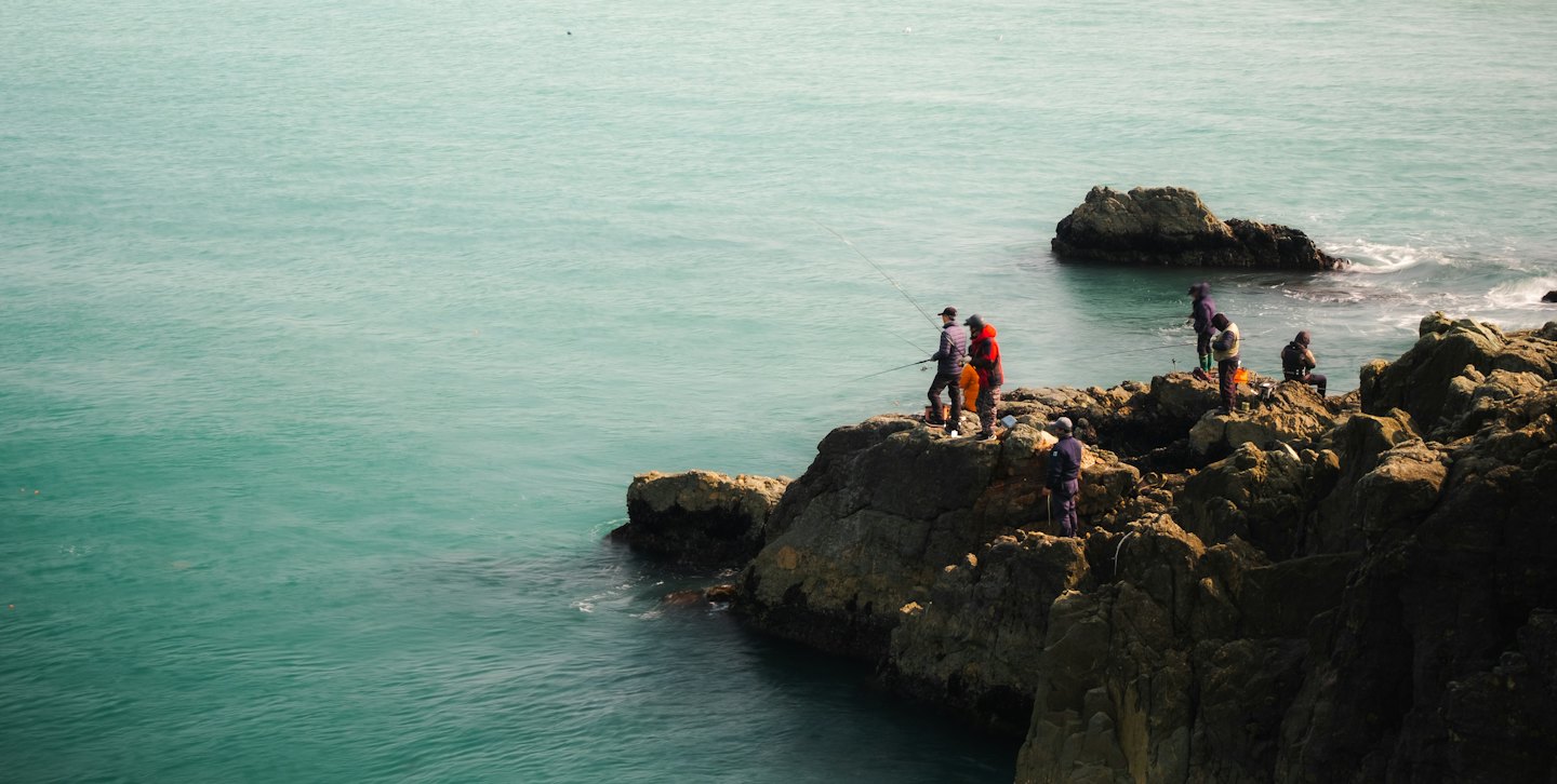 People fishing from the rocky ocean coastline.