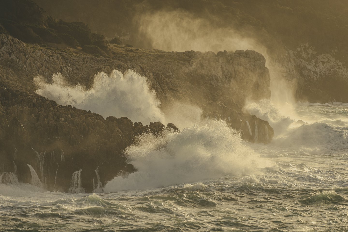Waves crash against dark rocky cliffs along the coast.